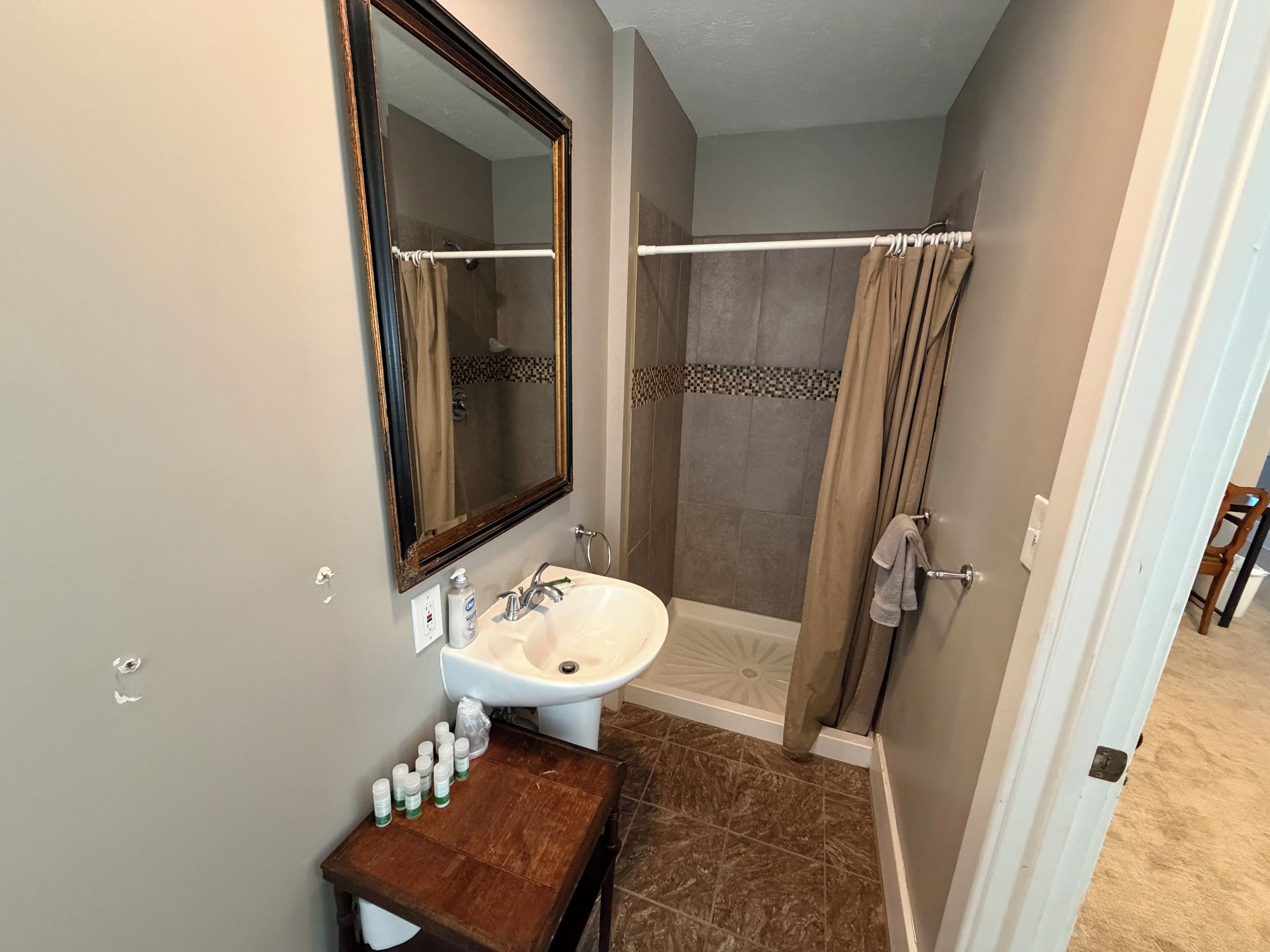 A bathroom with a sink, mirror, shower, and a towel rack.