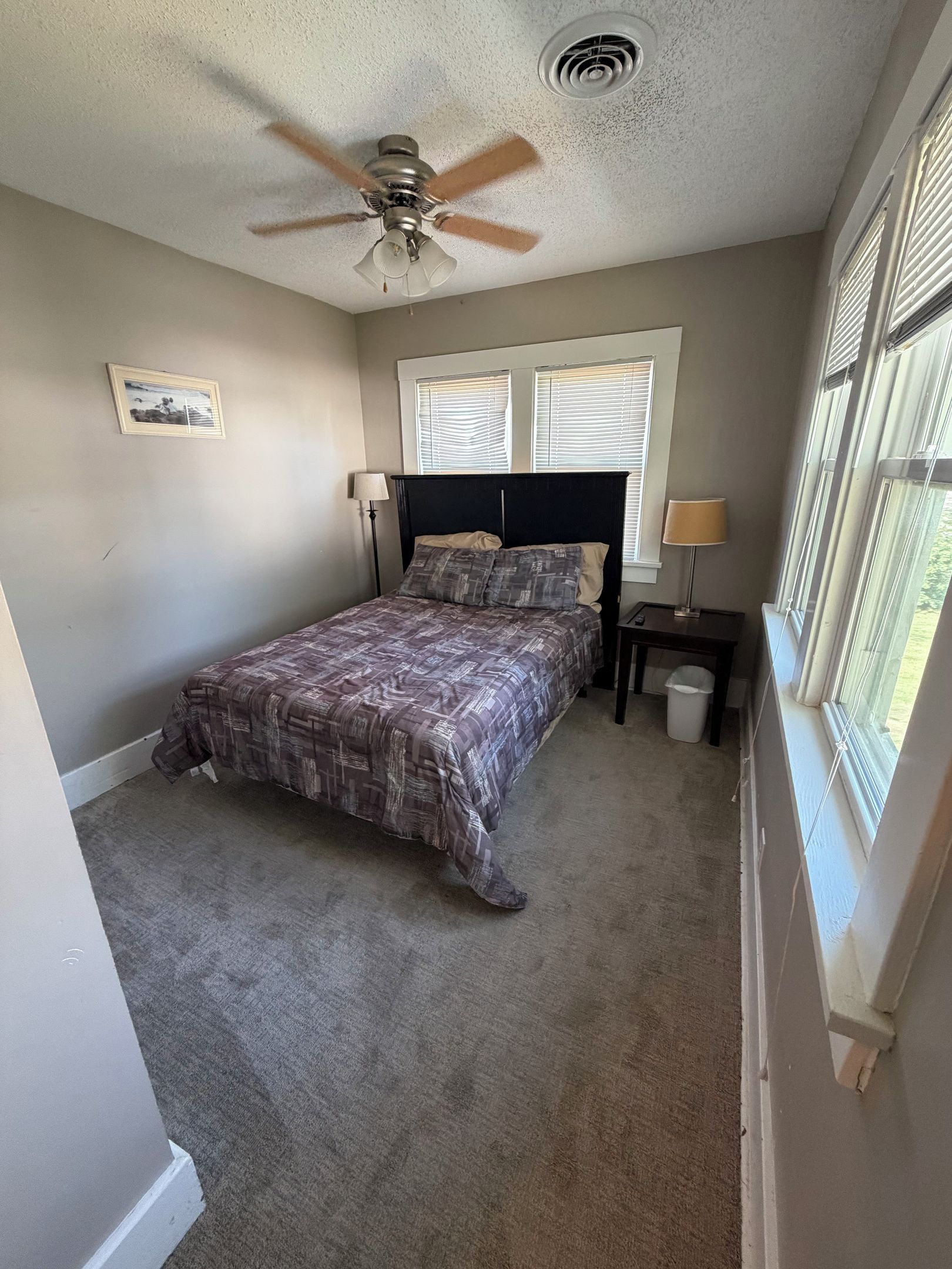 A bedroom with a bed, two bedside tables, a ceiling fan, and a window with blinds.
