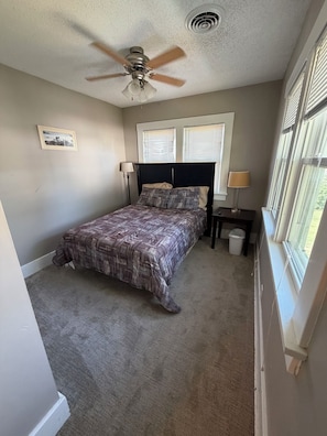 A bedroom with a bed, two bedside tables, a ceiling fan, and a window with blinds.