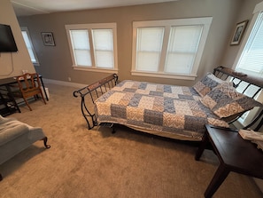 A bedroom with a bed, a chair, a table, and a television.