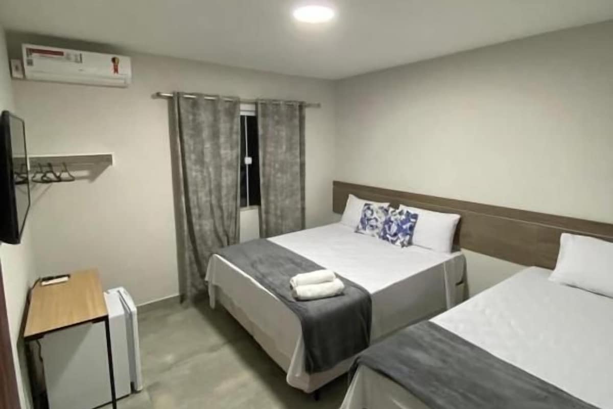 Quarto de hotel com duas camas, uma escrivaninha, uma cadeira e uma televisão.