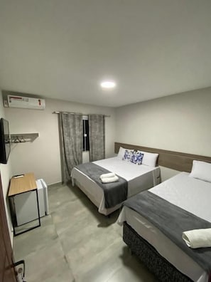 Quarto de hotel com duas camas, uma escrivaninha, uma cadeira e uma televisão.