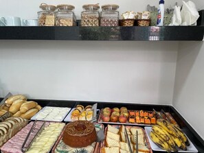 Buffet com diversos alimentos, incluindo pão, doces e frutas.