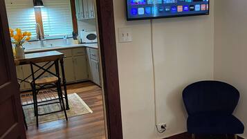 Una habitación con una cama, un televisor montado en la pared que muestra varios servicios de streaming, un sillón azul oscuro y piso de madera.