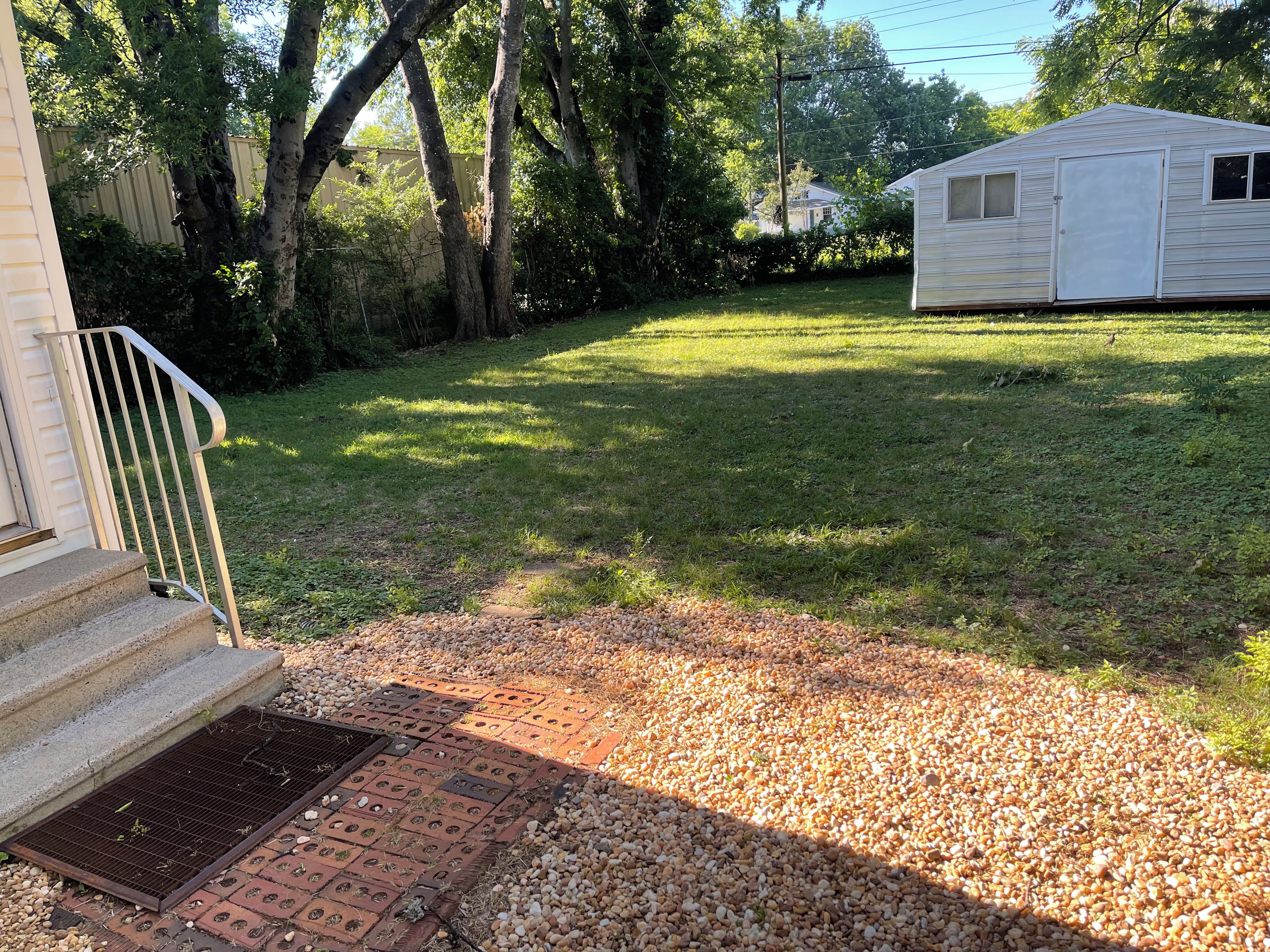 A residential property with a front yard, a small shed, and a staircase leading to a door.