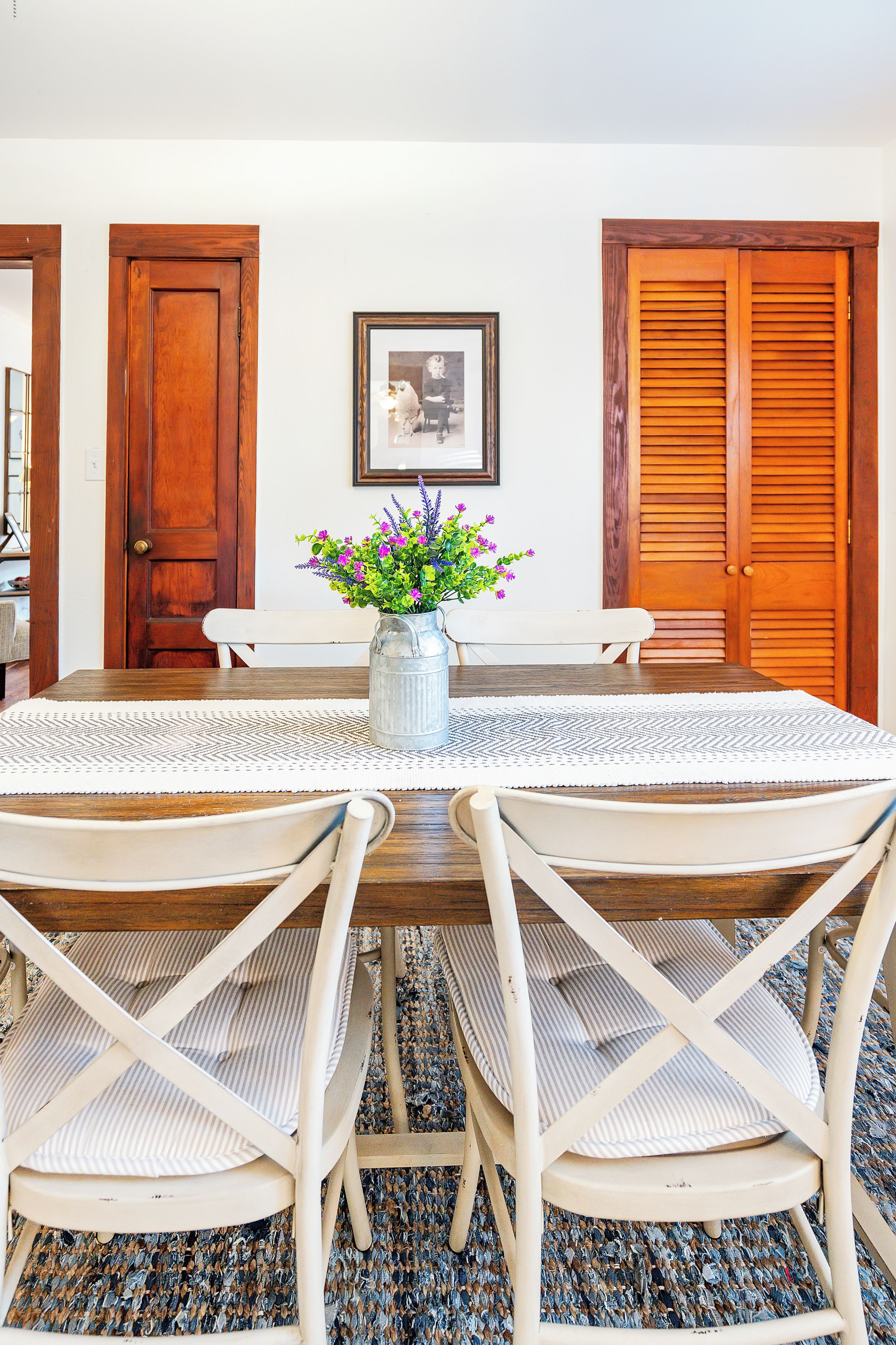 Un comedor con una mesa redonda, cuatro sillas, un jarrón con flores y dos puertas de madera.