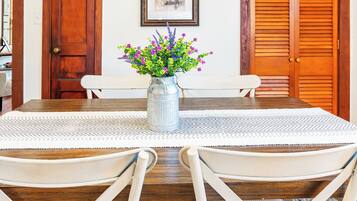 Un comedor con una mesa redonda, cuatro sillas, un jarrón con flores y dos puertas de madera.