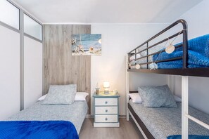 A compact bedroom with two bunk beds, a bedside table with a lamp, and a wall-mounted shelf with decorative items. - GuestReady - Casa Lali in front El Caleton Pool (La Matanza de Acentejo)