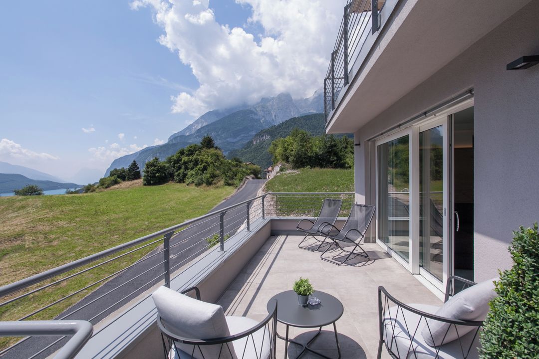 Un balcón con mobiliario exterior, una mesita y vistas a montañas y un lago.