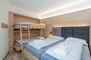 A bedroom with a bunk bed, a lower bed with a headboard, and a bedside table with a lamp. - CAMELIE APARTMENT - BELLAVISTA LAKE RESIDENCE (Trentino-Alto Adige)