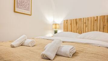 Ein Hotelzimmer mit einem Holz-Kopfteil, einem Bett mit weißer Bettwäsche, zwei zusammengerollten Handtüchern auf dem Bett und einer Wandlampe.