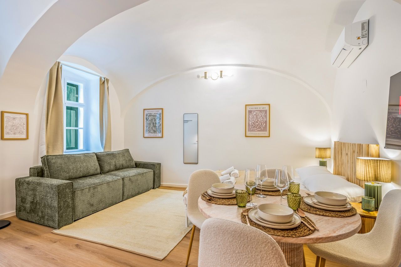 Ein modernes Wohnzimmer mit einer Couch, einem Esstisch für vier Personen und einem großen Fenster mit Vorhängen.
