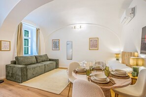 Ein modernes Wohnzimmer mit einer Couch, einem Esstisch für vier Personen und einem großen Fenster mit Vorhängen.