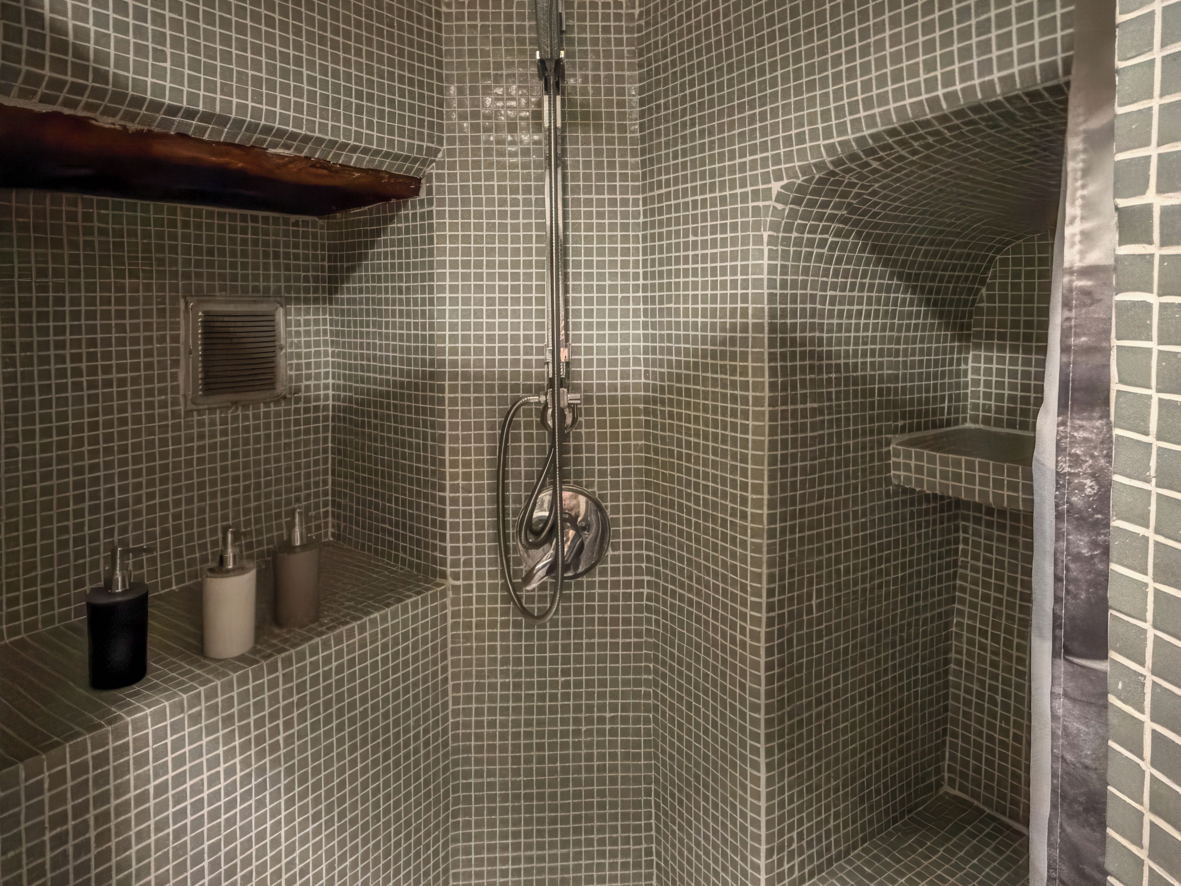 A shower area with a tiled wall, a handheld showerhead, and a shelf with toiletries.