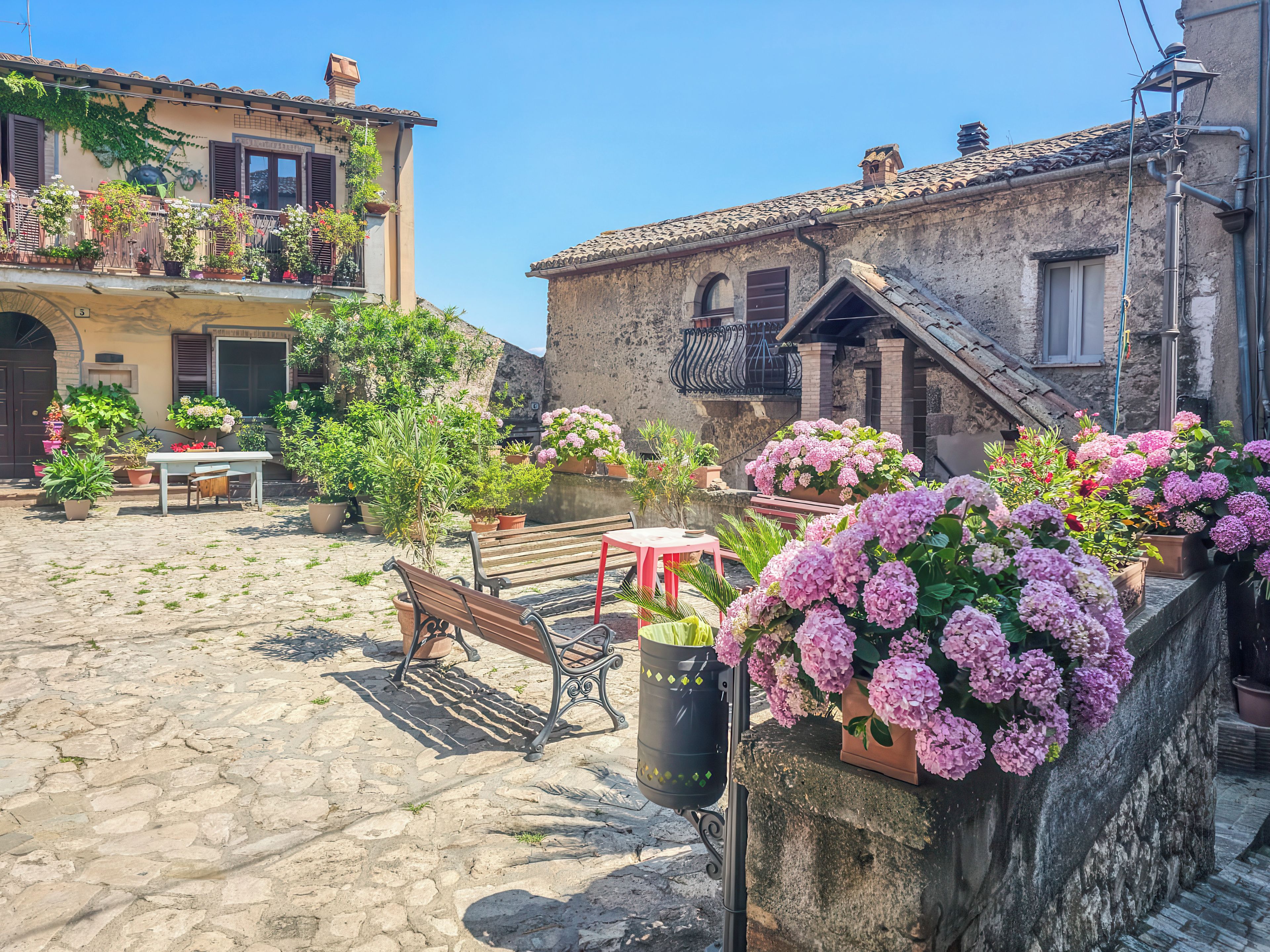 A courtyard with cobblestone flooring, a wooden bench, and potted plants.