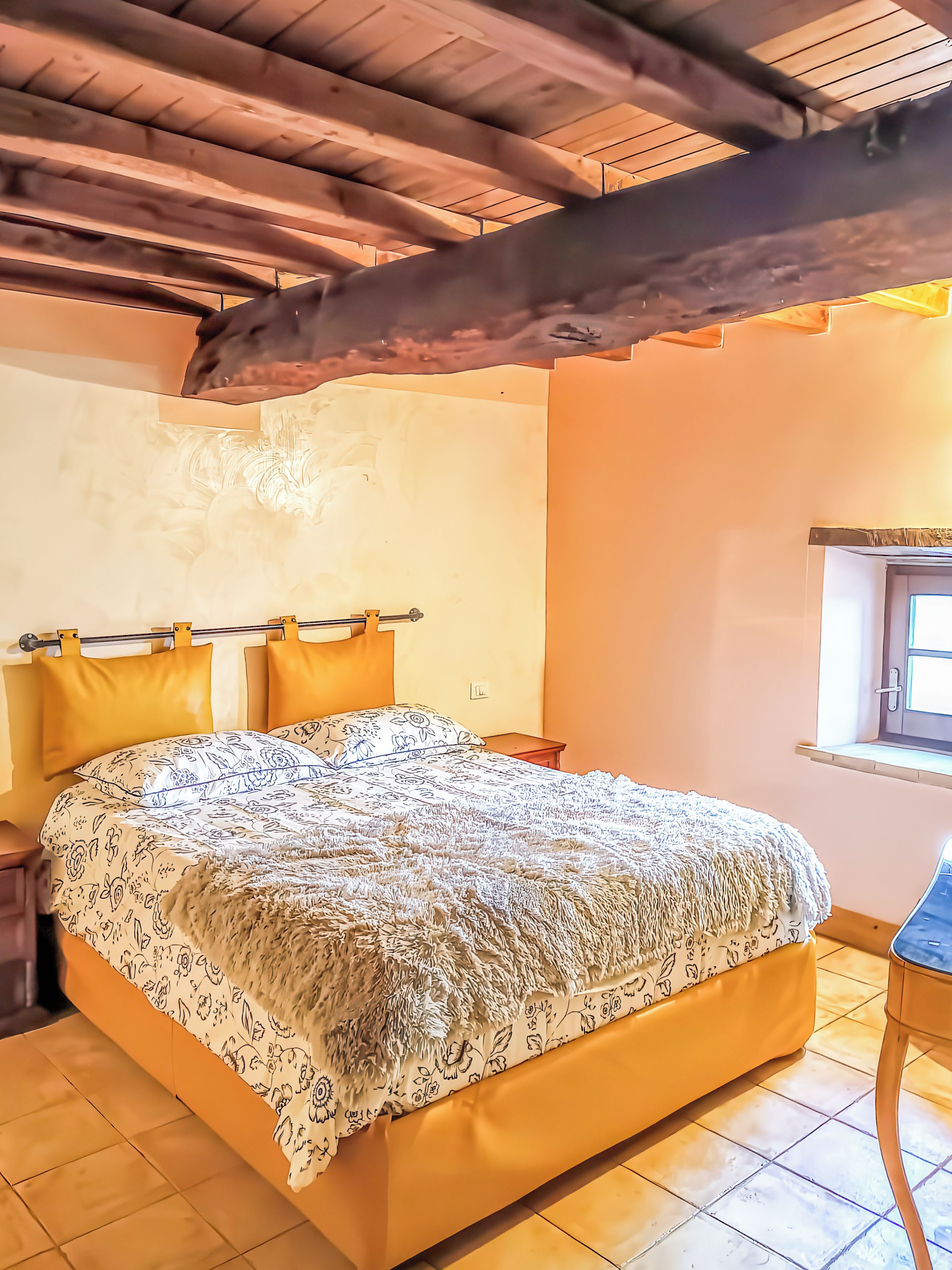 Ein Schlafzimmer mit Bett, Holzbalken, einem Fenster und einem Nachttisch.