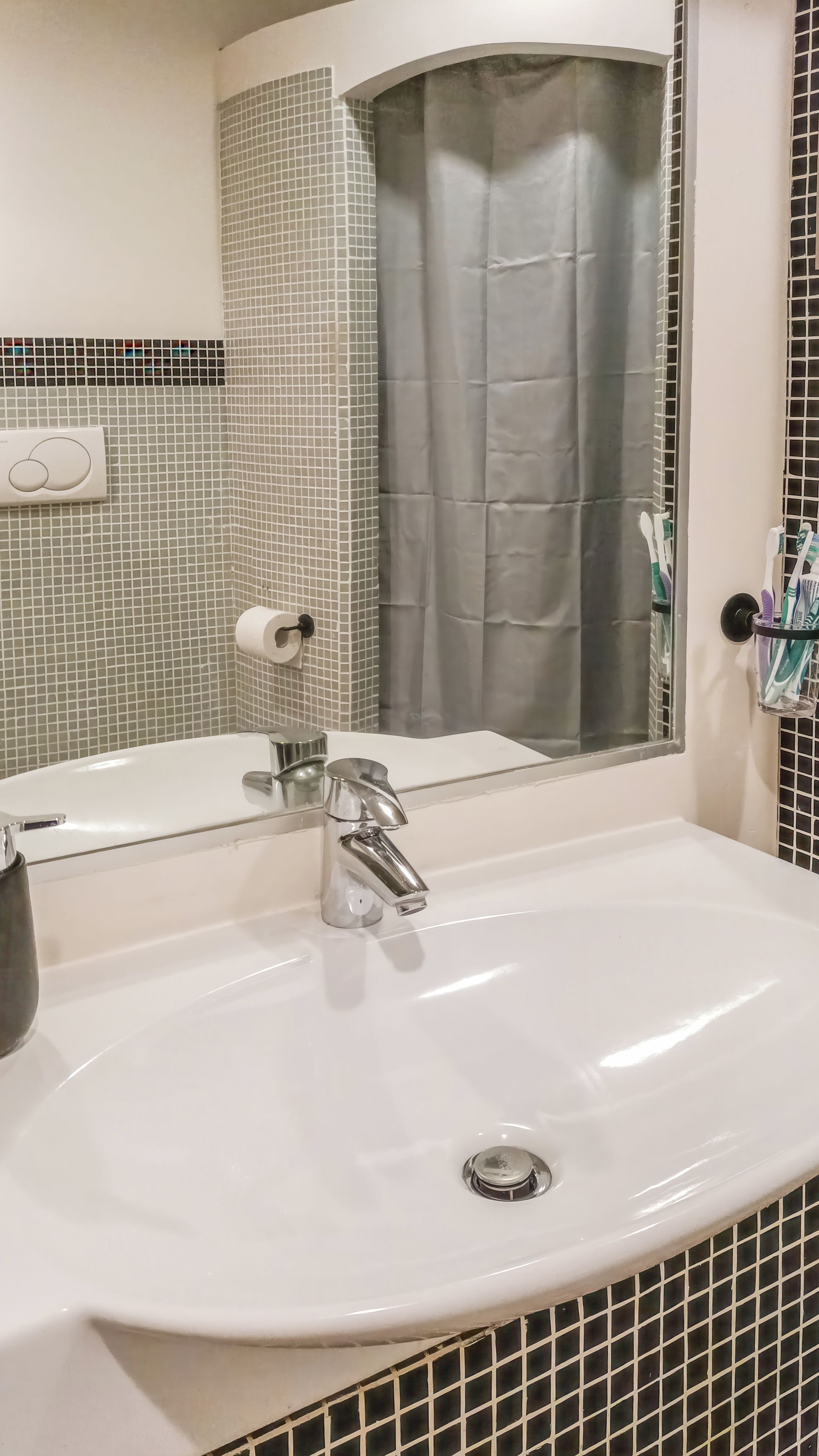A bathroom with a white sink, a mirror, a shower curtain, and a toothbrush holder.