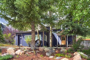 A two-story house with a dark blue exterior, a front porch, and a large tree in the front yard. - Abbett Placer Historic Cabin (Breckenridge)