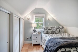 A bedroom with a sloped ceiling, a window with a view, a bedside table with a lamp, and a bed with patterned bedding. - Abbett Placer Historic Cabin (Breckenridge)