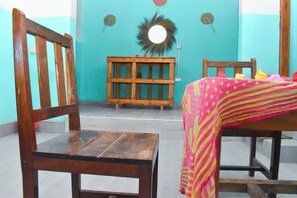 Una habitación con una silla de madera, una mesa con un mantel colorido y un banco de madera frente a una pared turquesa.