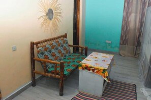 Una habitación pequeña con una silla de madera, una mesa pequeña y un cojín estampado.