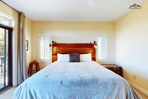 Ein Schlafzimmer mit einem großen Bett, zwei Fenstern mit Rollläden, einem Nachttisch und einem Koffer.