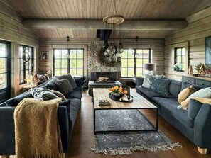 A cozy living room with a fireplace, two sofas, a coffee table with flowers, and large windows. - Log cabin with jacuzzi and Gaustatoppen views (Tinn Austbygd)