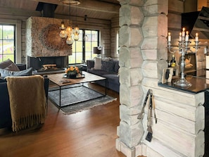 A cozy living room with a stone fireplace, a sofa, a coffee table, and a hanging light fixture. - Log cabin with jacuzzi and Gaustatoppen views (Tinn Austbygd)