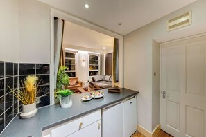 A modern kitchen with a dark countertop, white cabinets, and a view into the living room through an open door. - Prime 2BR Haven Harrods on your doorstep (Greater London)
