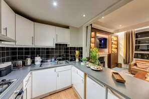 A modern kitchen with white cabinets, a black tiled backsplash, and a built-in oven. - Prime 2BR Haven Harrods on your doorstep (Greater London)