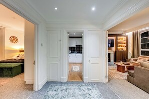 A hallway leading to a kitchen and living area with a sofa and a TV. - Prime 2BR Haven Harrods on your doorstep (Greater London)