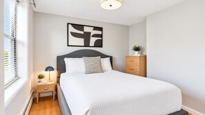 A bedroom with a bed, a nightstand, a lamp, a dresser, and a wall-mounted abstract art piece. - Private Apt Walk to Shops/Restaurants (Boston, MA)