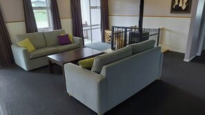 A living room with a grey sofa, a coffee table, and a dining table with chairs. - Expansive 6 Bedroom House. Fully fenced short walk to the River or Town Center (Tūrangi)