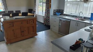 Een keuken met een houten kookeiland, roestvrijstalen apparatuur en een eethoek met stoelen.