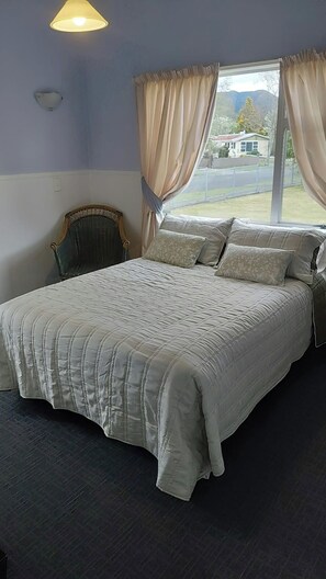 A bedroom with a bed, curtains, a chair, and a window with a view. - Expansive 6 Bedroom House. Fully fenced short walk to the River or Town Center (Tūrangi)
