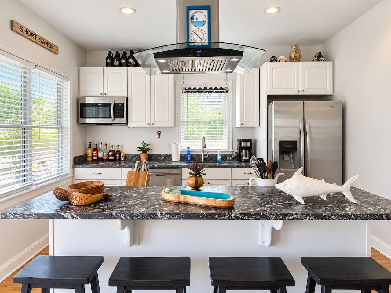 Una cocina moderna con armarios blancos, un refrigerador de acero inoxidable, un microondas integrado y una isla grande con taburetes de bar.