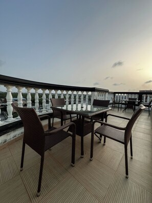 Eine Dachterrasse mit Glastisch, Korbstühlen, einem Geländer und Blick auf die Stadt.