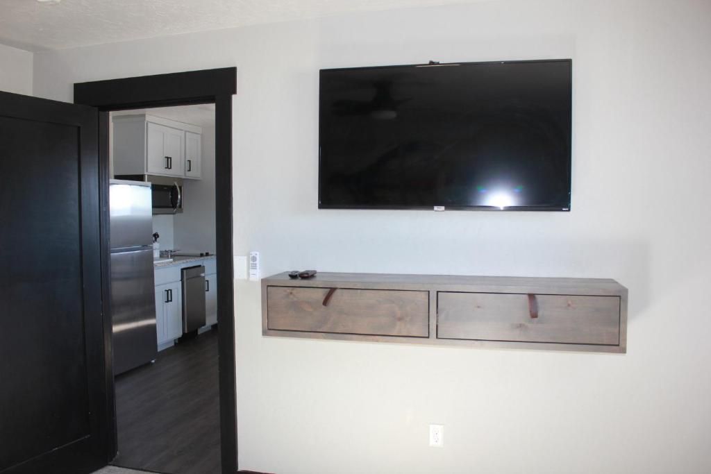 Una cocina moderna con electrodomésticos de acero inoxidable, un televisor de pantalla plana montado sobre un mueble de madera y una puerta oscura que da a otra habitación.