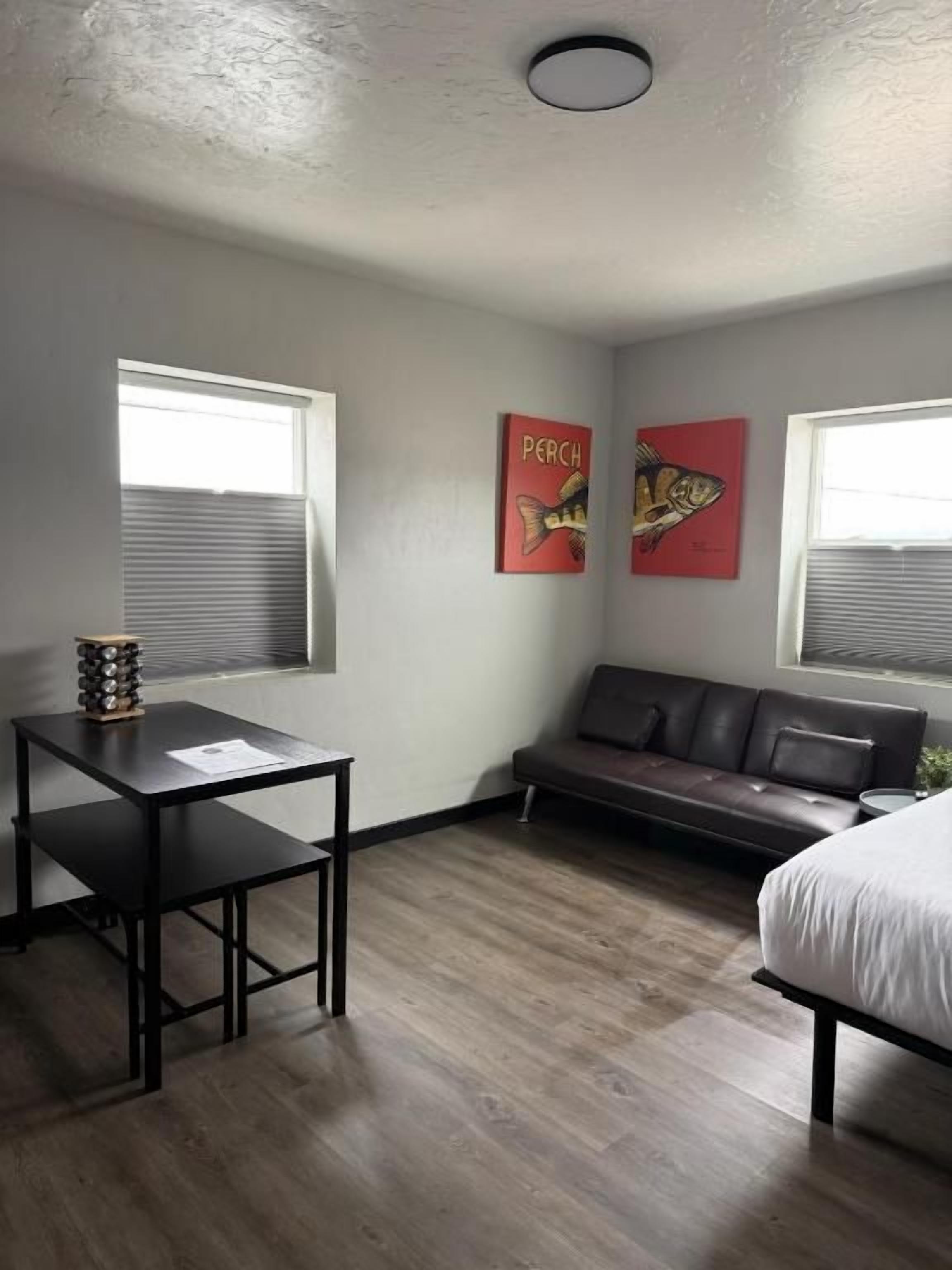 Una habitación con cama, sofá, mesa y dos ventanas con persianas.