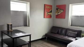 Una habitación con cama, sofá, mesa y dos ventanas con persianas.