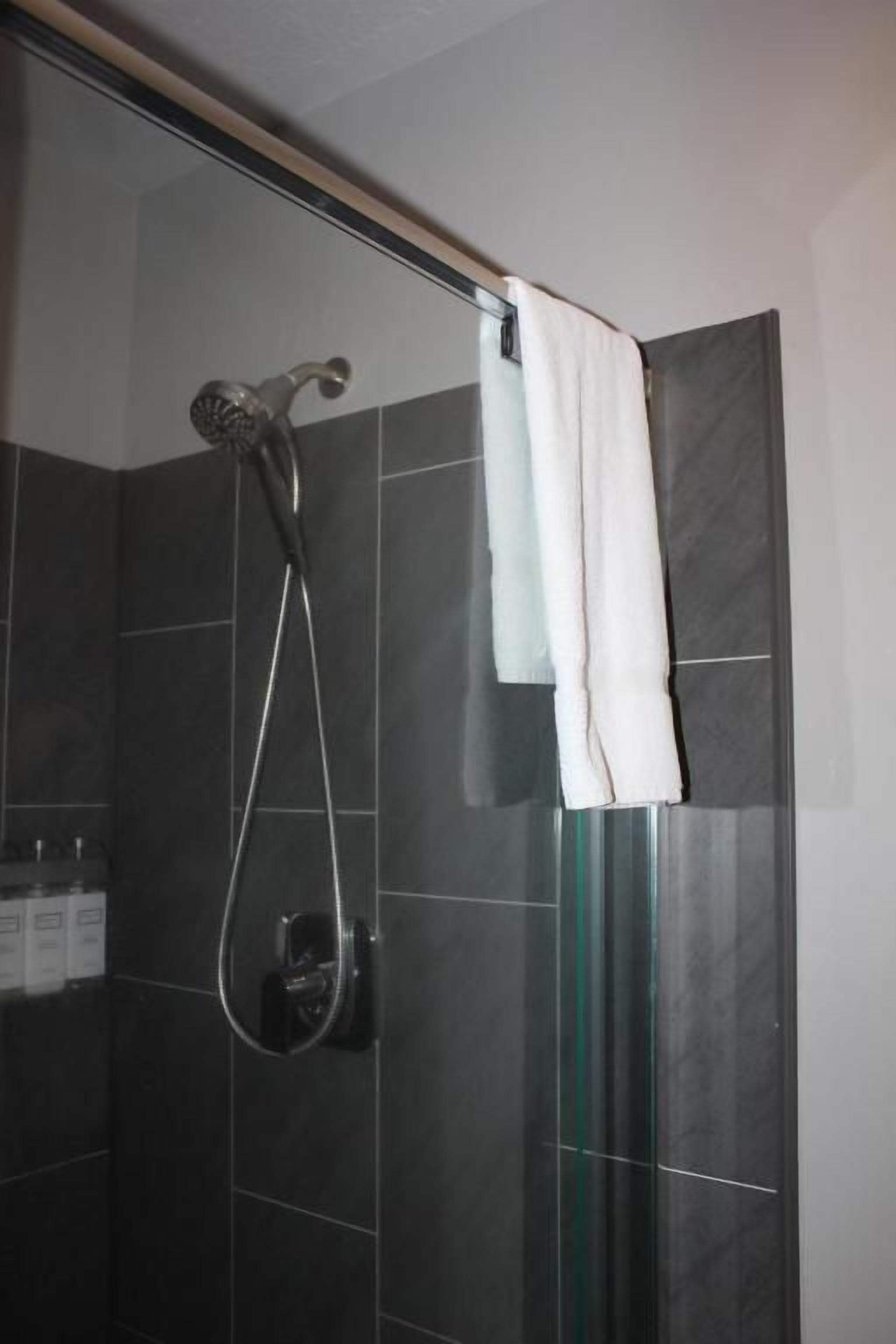 Eine Dusche mit Glastür, Duschbrause zum Händchenhalten und ein weißes Handtuch, das an der Tür hängt.
