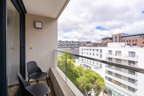 A balcony with two chairs, a view of a cityscape, and a building with a sign. - Newlands Peak 1 Bedroom Apartment (Cape Town)