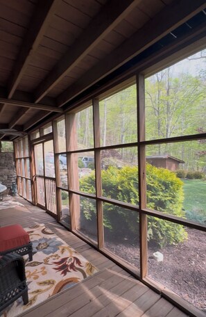 A covered porch with large windows, a red cushioned bench, and a patterned rug. - Good Life Ridge- 38 Acres of Dog-Friendly Heaven (Mars Hill)