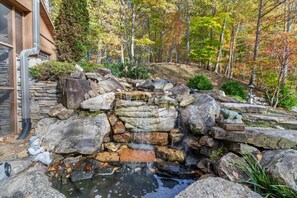 A stone waterfall feature with a small pond, surrounded by rocks and vegetation. - Good Life Ridge- 38 Acres of Dog-Friendly Heaven (Mars Hill)
