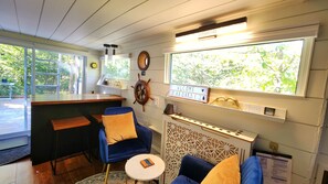 Quarto aconchegante com área de bar, uma cadeira azul, uma mesa pequena e um painel decorativo com um leme e uma placa de boas-vindas.