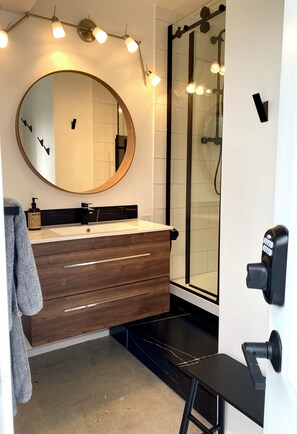 A bathroom with a round mirror, wooden vanity, black shower enclosure, and a towel rack. - Peaceful Relaxation - Houseboat & Fall Foliage (Stone Mills)
