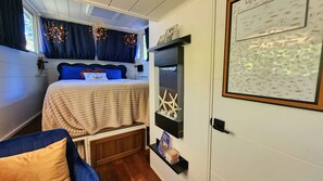 A cozy bedroom with a bed, a small shelf with decorative items, and a wall with a word cloud. - Peaceful Relaxation - Houseboat & Fall Foliage (Stone Mills)