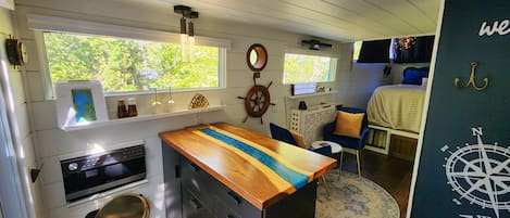 A compact kitchen with a wooden countertop, a stove, and a sink. There is a window with a view of greenery outside.