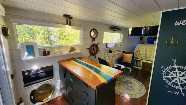 A compact kitchen with a wooden countertop, a stove, and a sink. There is a window with a view of greenery outside.