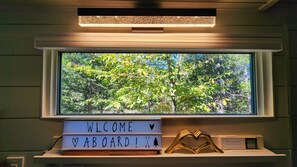 Janela com vista para árvores, uma placa de boas-vindas e um objeto em formato de coração em uma prateleira.